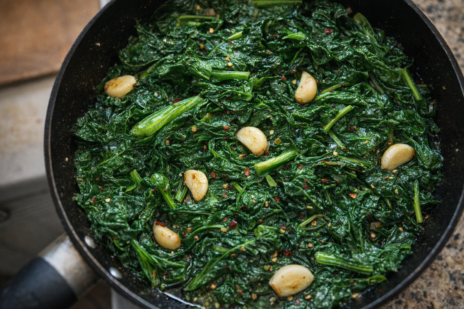 A close-up, top-down shot of sauteed Swiss chard with garlic in a skillet, vibrant green leaves, glistening with olive oil, garlic cloves visible, sprinkle of red pepper flakes, warm lighting